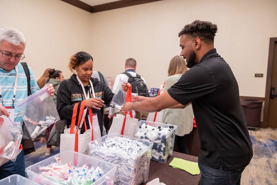 People inside and looking at supplies on table for a community event.