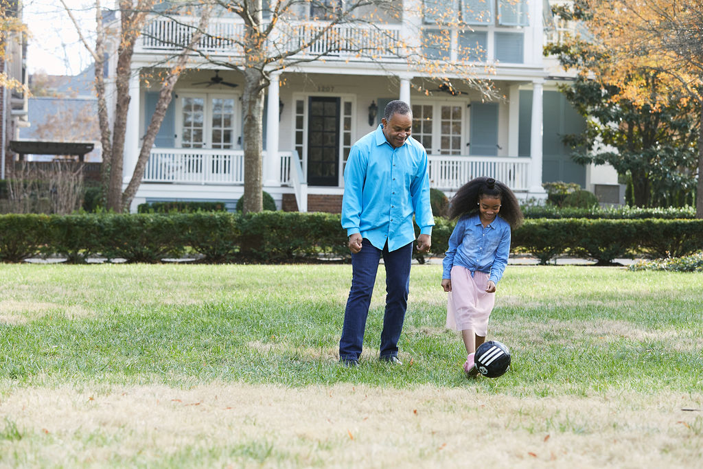 Grandfather and Granddaughter playing soccer in the front yard.